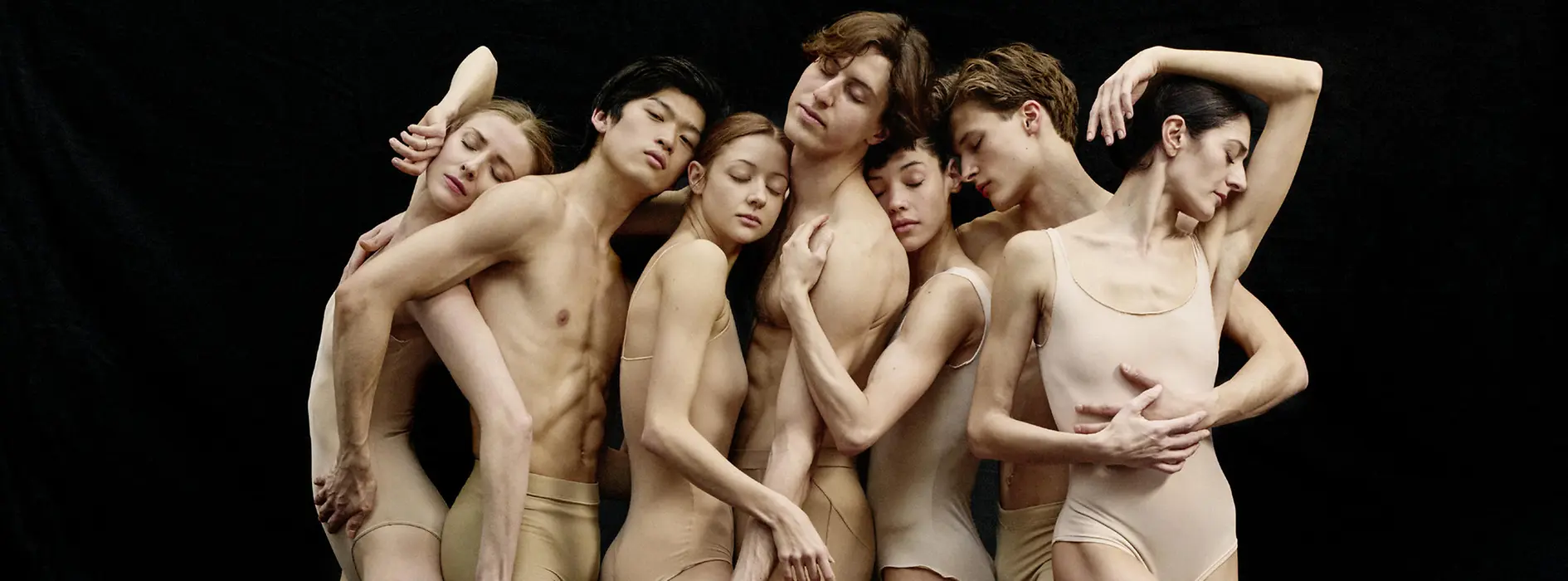 Sieben Ballettänzerinnen und -tänzer eng beieinander stehend in Pose.