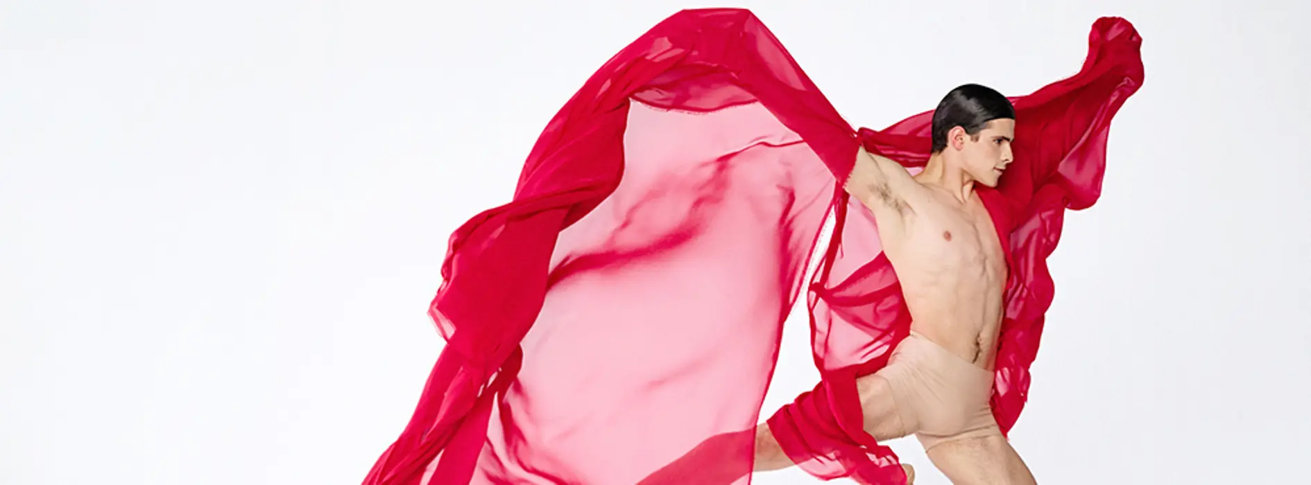 Danseur en plein saut, tenant dans chaque main un tissu rouge transparent qui flotte autour de lui.