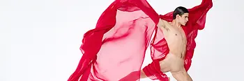 Danseur en plein saut, tenant dans chaque main un tissu rouge transparent qui flotte autour de lui.