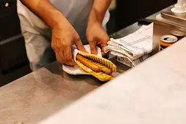 Two hands wrapping a Bosna sausage in a napkin