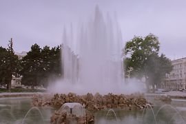 Hochstrahlbrunnen: eine Wasserfläche, dahinter Steine, dahinter ein senkrechter Wasserstrahl