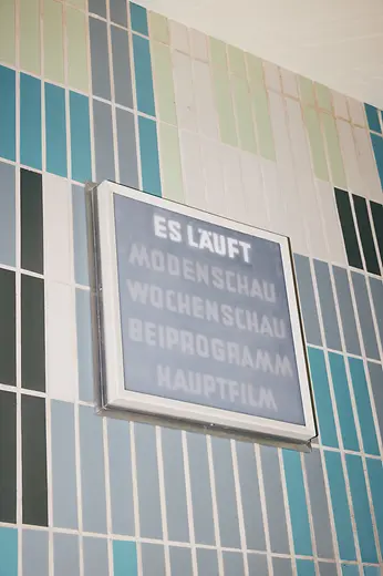 Gartenbaukino interior shot, light sign with wording \"ES LÄUFT\" (\"IT'S RUNNING\")