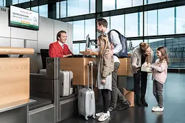 Eine Familie mit zwei Mädchen beim Einchecken am Check-In-Schalter von Austrian Airlines 