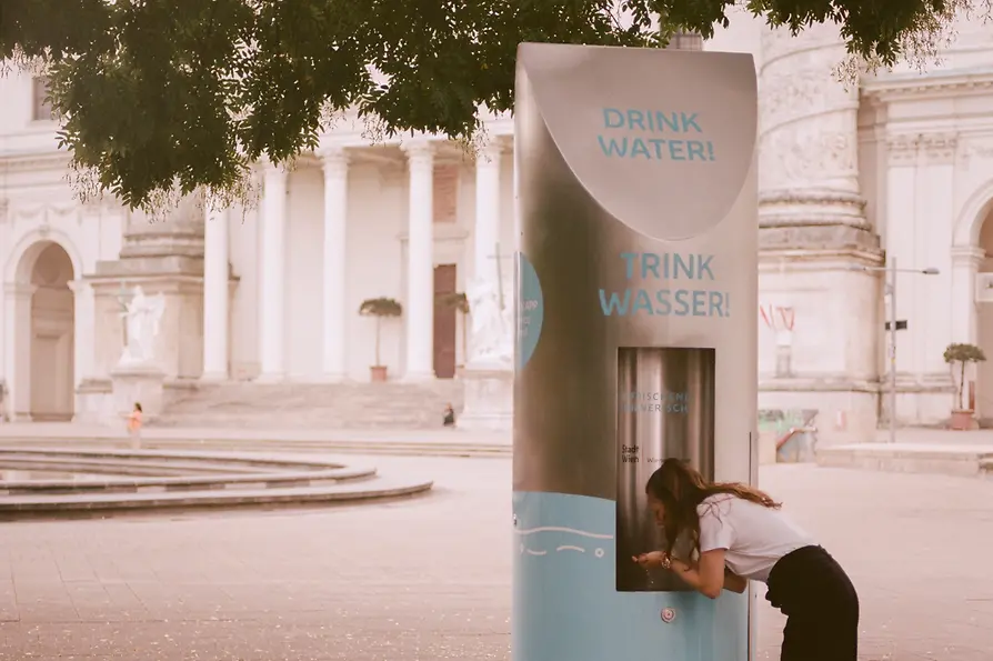 Une femme boit à une fontaine avec l'église Saint-Charles à l'arrière-plan