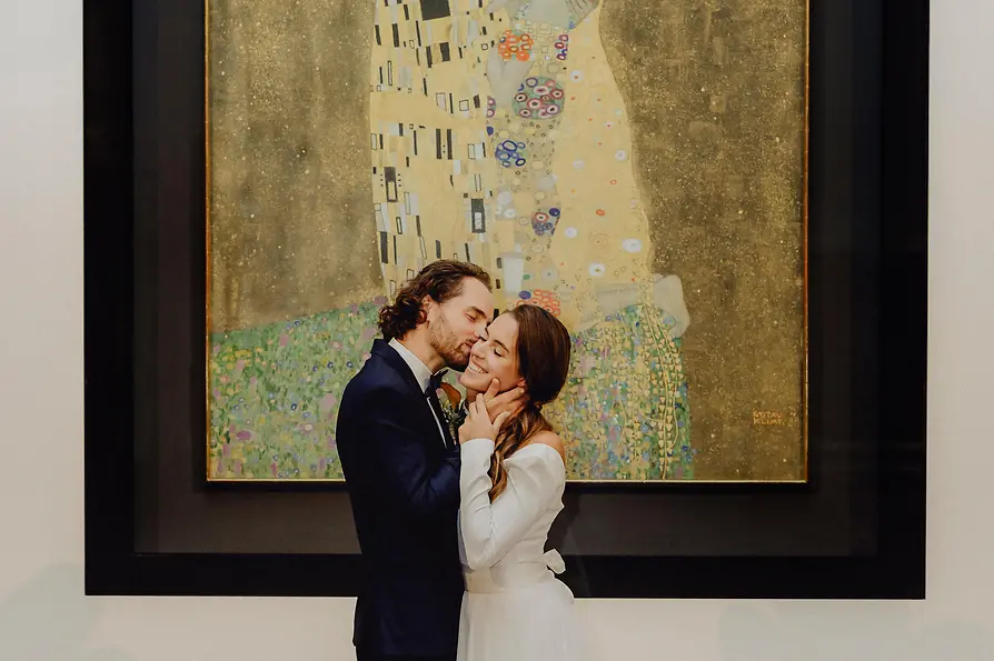 A Couple kissing in front of the painting the Kiss from Gustav Klimt