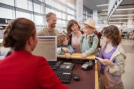Eine junge Familie mit drei Kindern beim Austrian Check-In-Schalter am Flughafen Wien