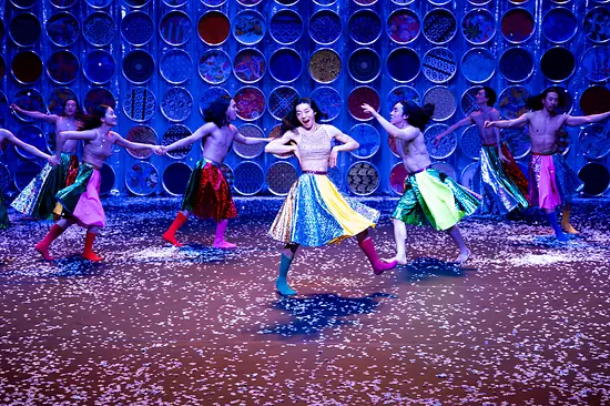 Koreanische Tänzer:innen wirbeln in bunten Röcken und Stiefeln auf der Bühne herum.