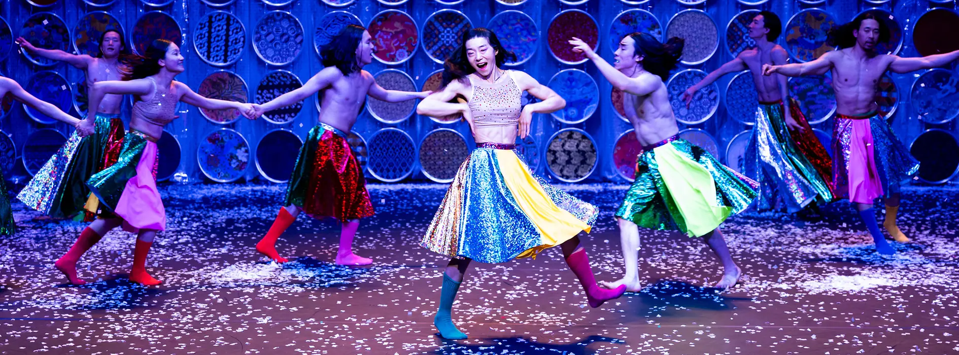 Koreanische Tänzer:innen wirbeln in bunten Röcken und Stiefeln auf der Bühne herum.