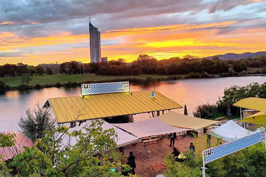 Schanigarten, Usus am Wasser, Wiener Skyline mit Sonnenuntergang im Hintergrund