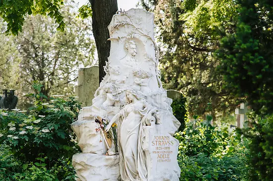 Marmornes Grabmal von Johann Strauss Sohn mit seinem Kopf als Relief, dazu im aufragenden Monument eine Frauenfigur, Fledermaus und ein Geige spielendem Engel.