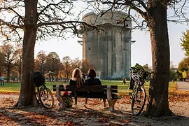 Two people sitting on a bench facing the flak tower in Augarten park
