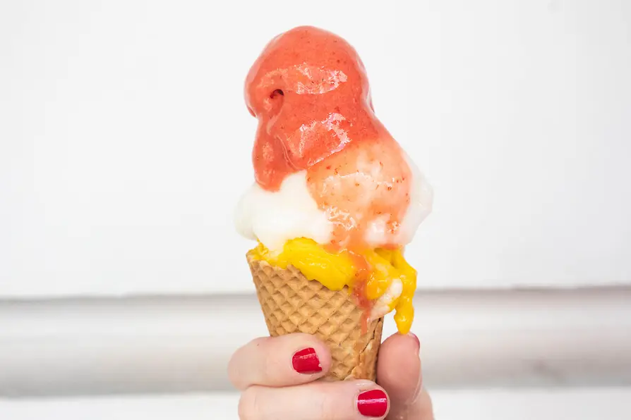 Mano con unghie smaltate di rosso che tiene un cono gelato con tre palline, fotografato a Vienna